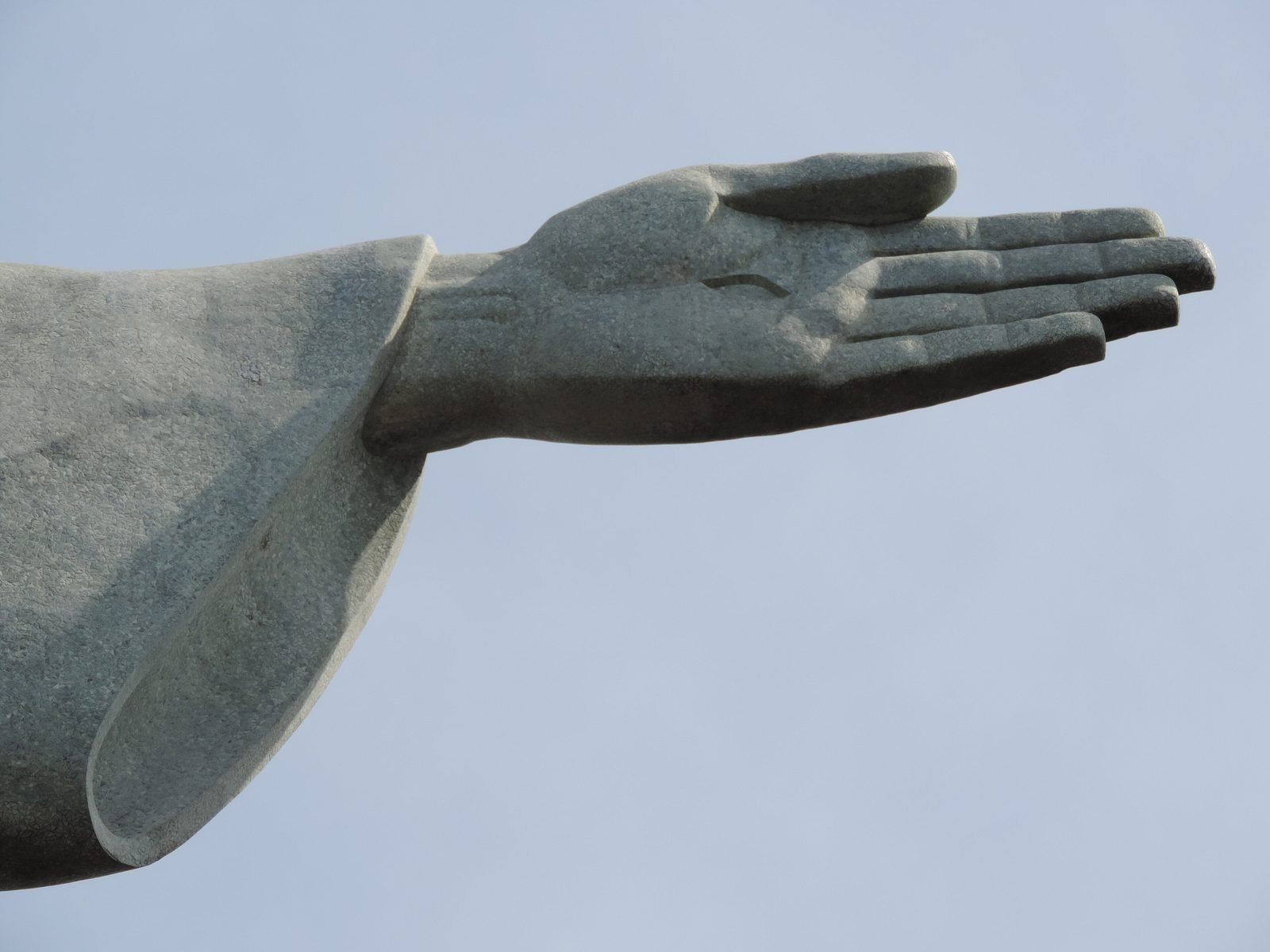 Mão aberta do Cristo Redentor, na ponta do braço, contra o céu