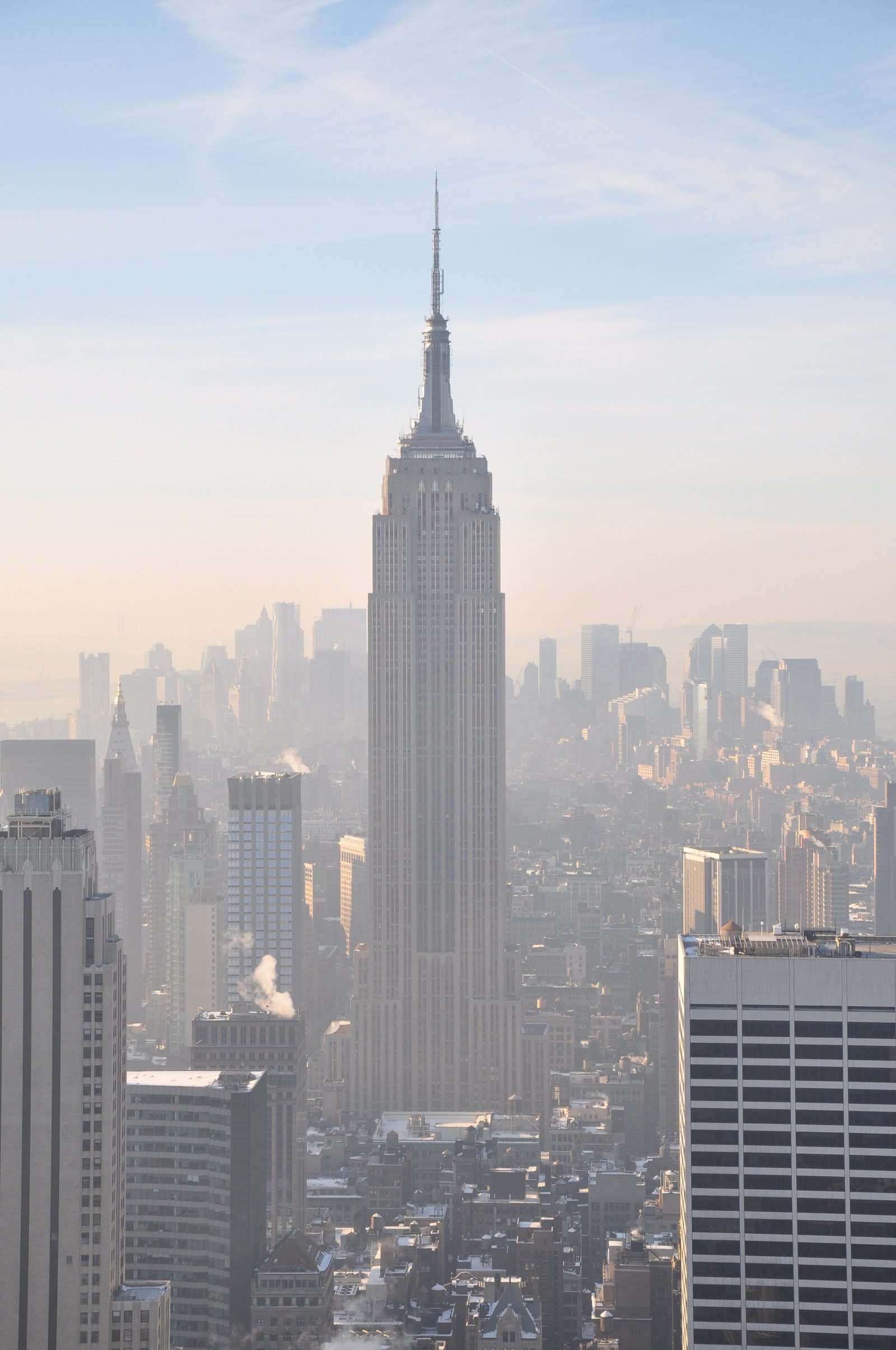 O Empire State Building visto do alto, com a antena no topo, entre os prédios de Manhattan numa manhã de névoa