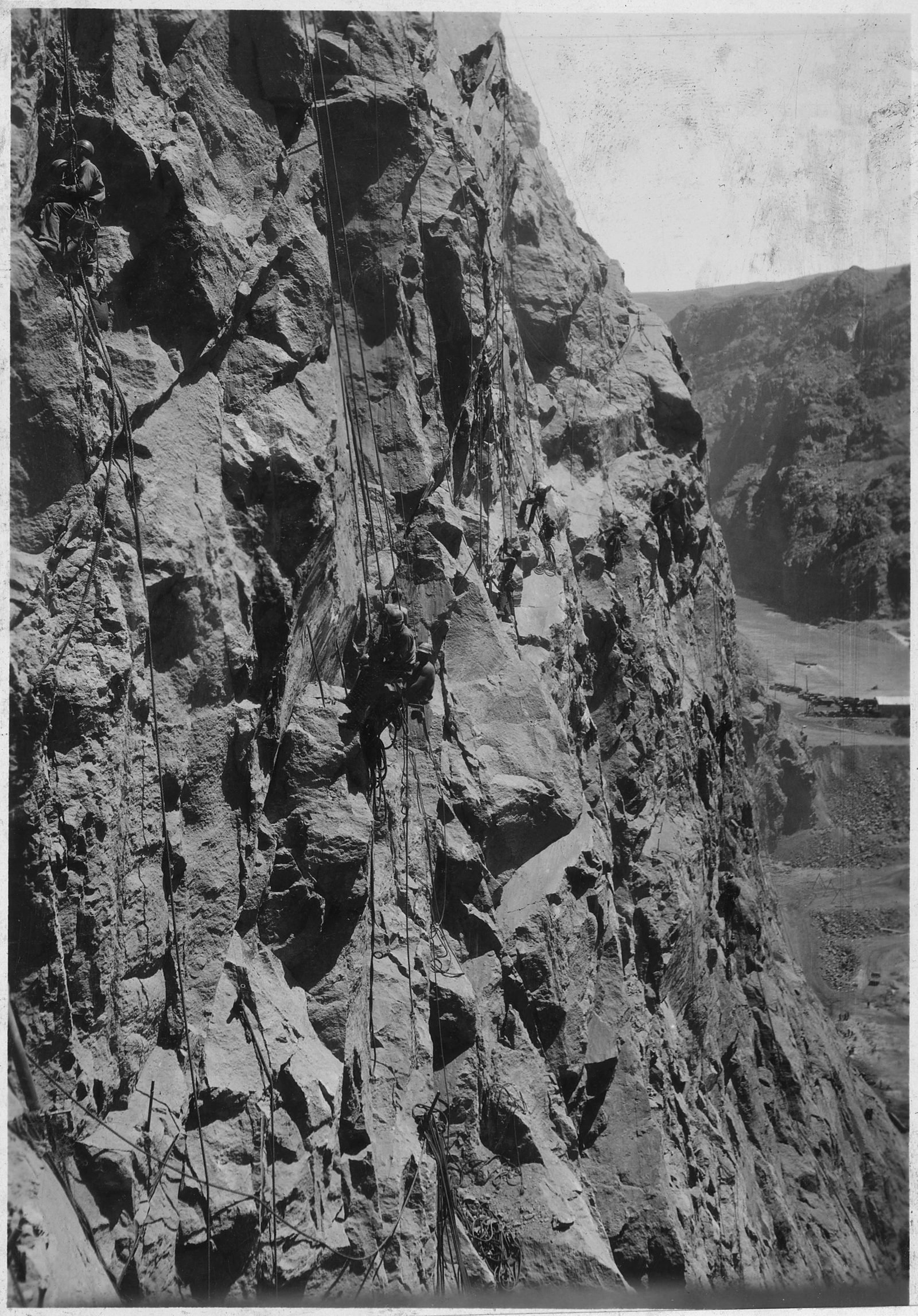 Homens pendurados por cordas num paredão vertical de rocha do cânion